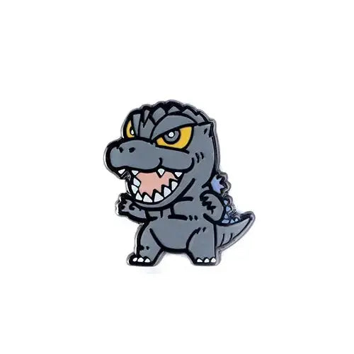 A cartoon-style Godzilla enamel pin on a plain white background. The pin features a gray dinosaur with yellow eyes, white teeth, and a pink mouth interior, outlined in black metal.