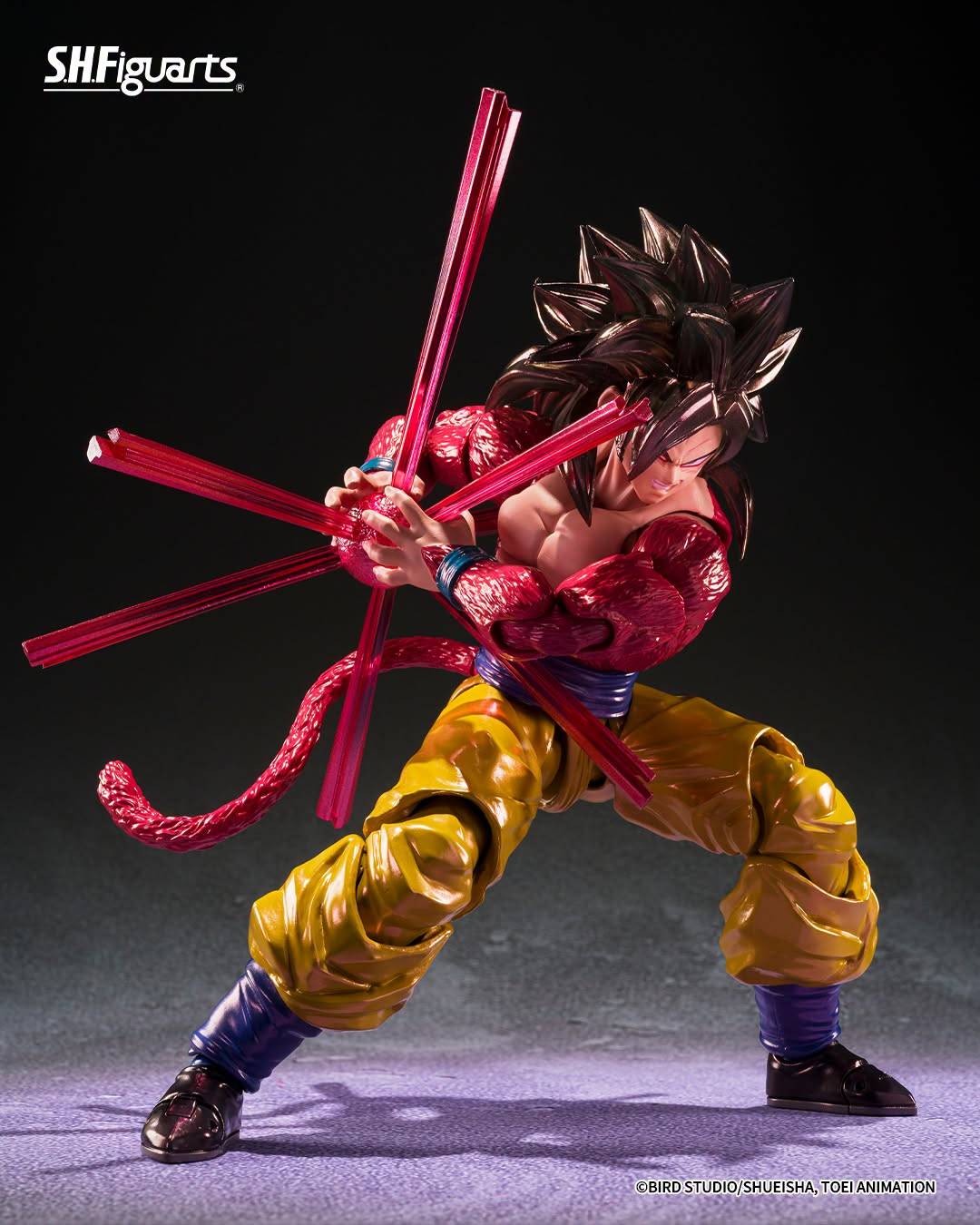 SH Figuarts Super Saiyan 4 goku action figure from Dragon Ball gt, standing in a dynamic pose with arms crossed over his chest. The figure features his signature metallic gold gi pants, a blue waistband, a pink Super Saiyan hairpiece, and a long pink tail, set against a dark studio background.