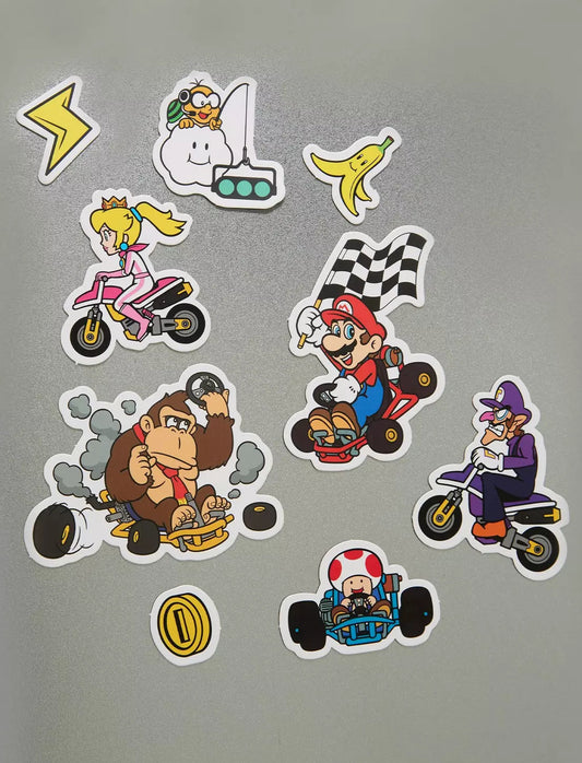 A set of colorful Super Mario-themed go-kart stickers displayed on a gray surface. The stickers feature characters like Mario, Princess Peach, Donkey Kong, Bowser, Luigi, Toad, and a banana peel.