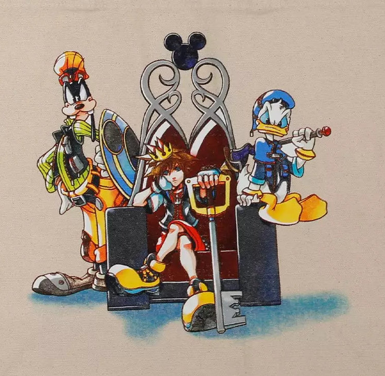 A beige canvas tote bag featuring a colorful graphic print of Disney Kingdom characters including Goofy, Donald Duck, and Pluto standing in front of a silver throne.