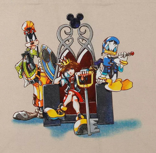 A beige canvas tote bag featuring a colorful graphic print of Disney Kingdom characters including Goofy, Donald Duck, and Pluto standing in front of a silver throne.