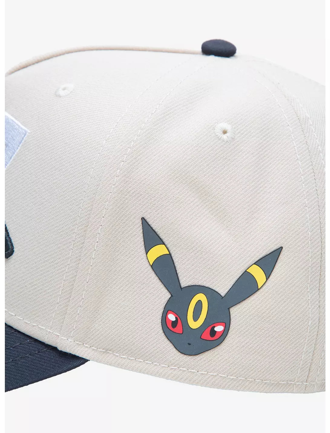 A structured baseball cap with a cream-colored crown, dark gray brim, and black embroidered Pokemon umbreon Japanese characters over large white and black  numerals on the front.