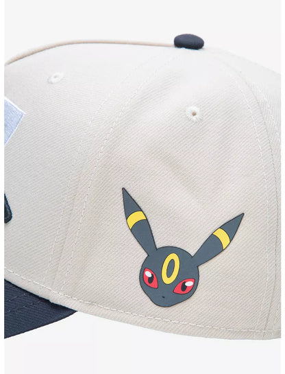 A structured baseball cap with a cream-colored crown, dark gray brim, and black embroidered Pokemon umbreon Japanese characters over large white and black  numerals on the front.