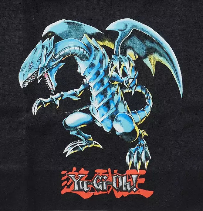 A black canvas tote bag featuring a large graphic print of the Yu-Gi-Oh! character Yugi's blue dragon, with red Yu-Gi-Oh! logo text underneath, shown against a plain white background.