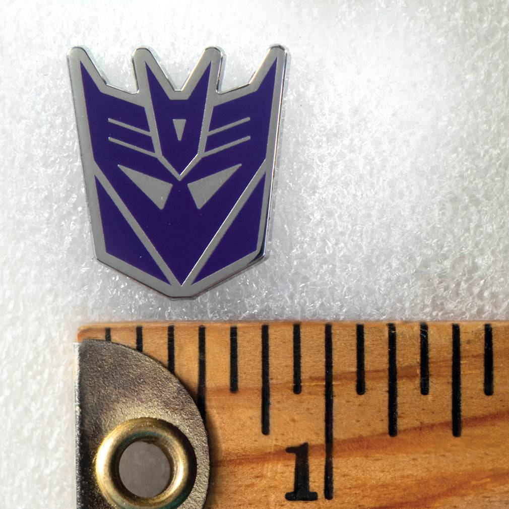 Decepticon logo from Transformers on a white background with a ruler for scale.