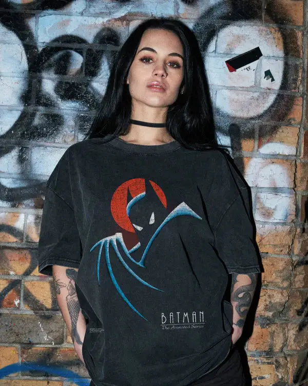 Person wearing a black Batman t-shirt in front of a graffiti-covered wall.