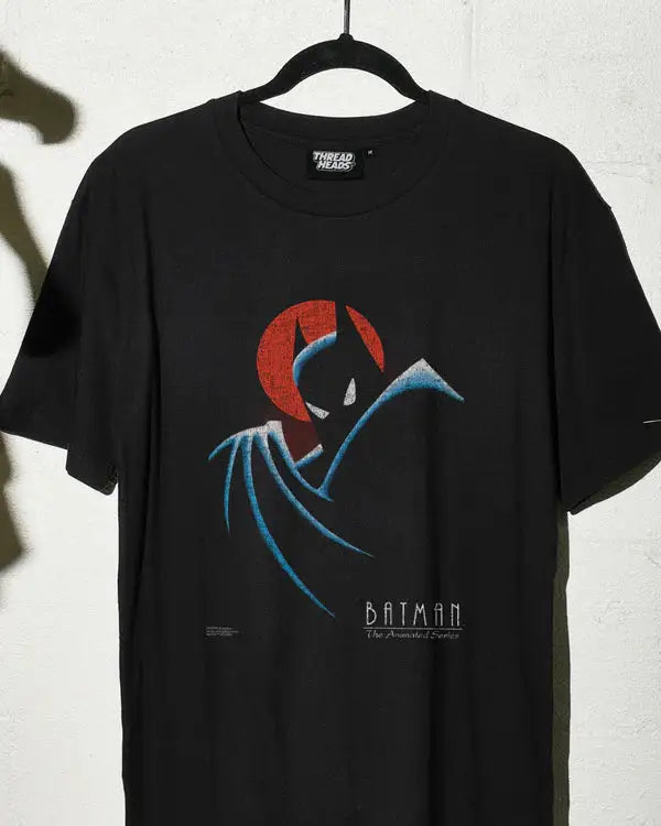 Black t-shirt with Batman logo on a hanger against a white wall