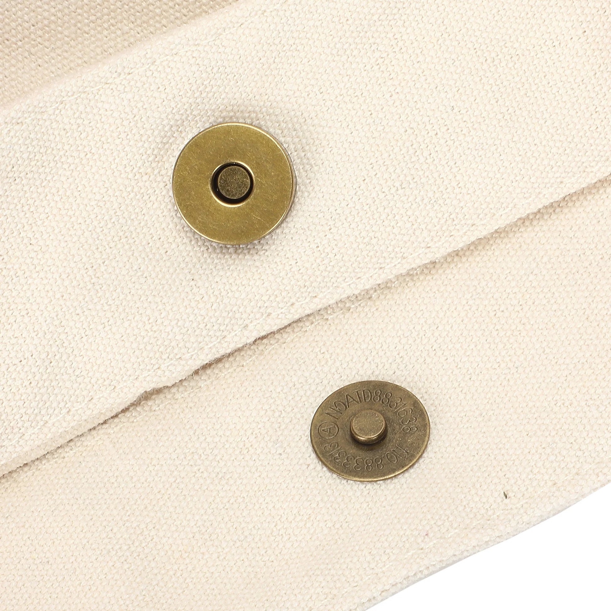 Close-up of a cream canvas sleeve or pouch with two round brass snap buttons, showing the textured fabric and metal hardware details.