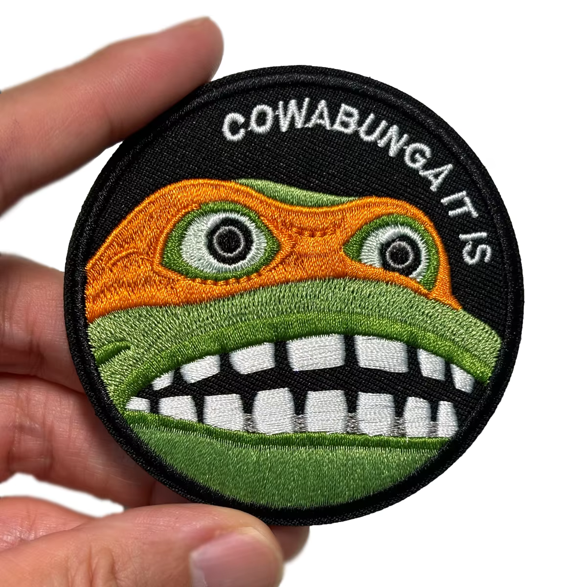 Circular patch of Teenage Mutant Ninja Turtles TMNT Michelangelo with a cartoonish face and 'Cowabunga It Is' text on a white background
