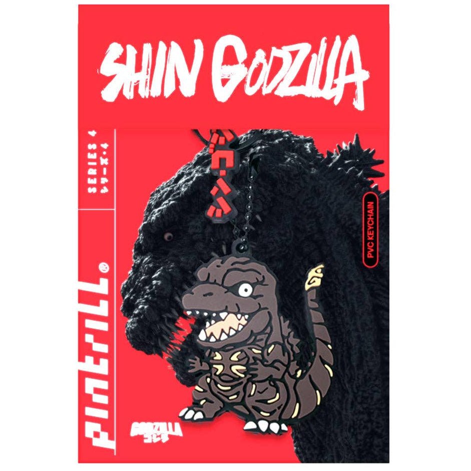 A chibi cartoon-style keychain featuring shin Godzilla character charm with yellow markings, attached to a black ball chain and clasp, with red Japanese text hanging above.