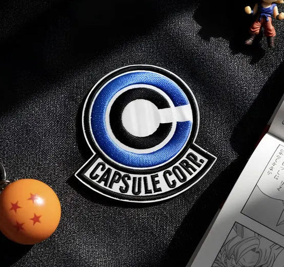 Keychain with a 'Capsule Corp' logo and a small figurine on a dark surface.