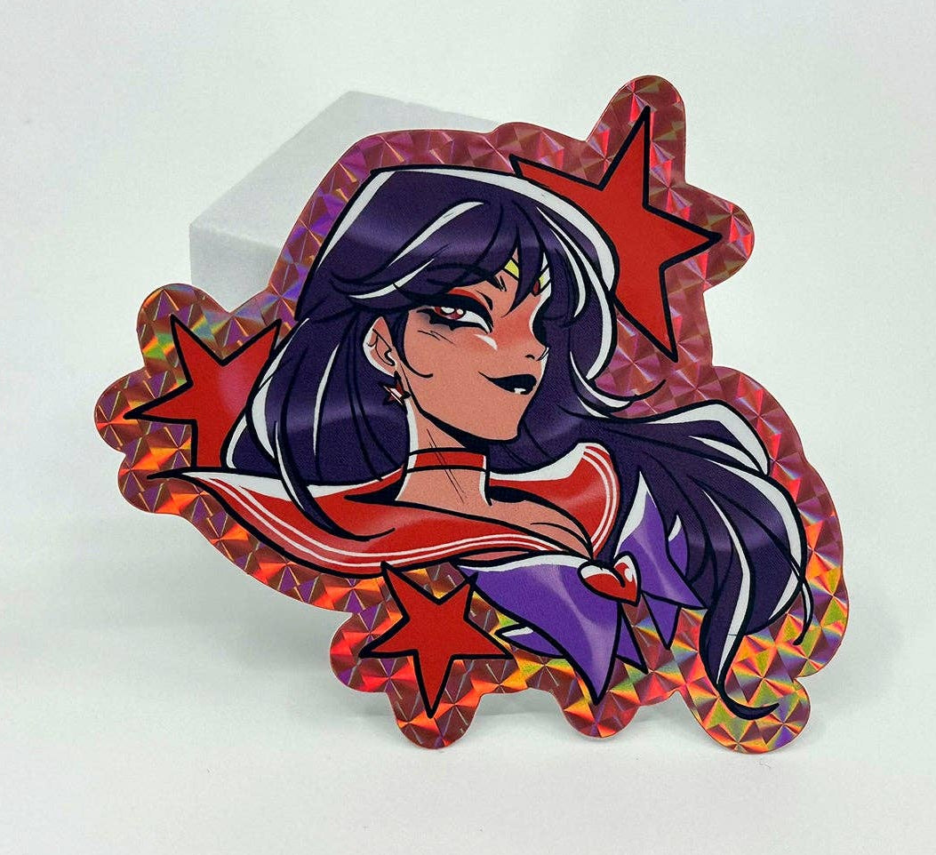 A die-cut holographic sticker featuring an anime-style Sailor moon Sailor scout Mars character with long dark purple hair, wearing a red and purple outfit, surrounded by red stars, displayed on a white background.