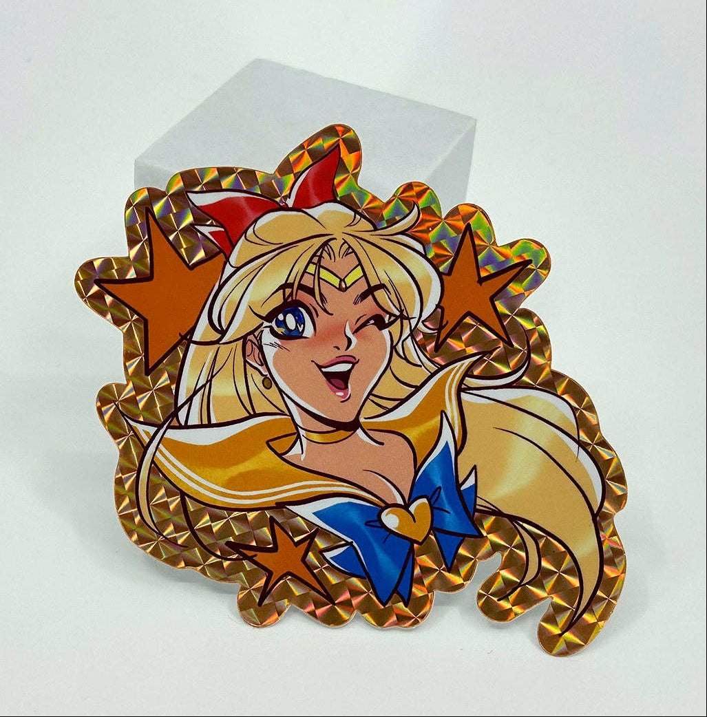 An anime Sailor Moon Sailor Scout Venus holographic sticker displayed on a small white block against a clean white background.