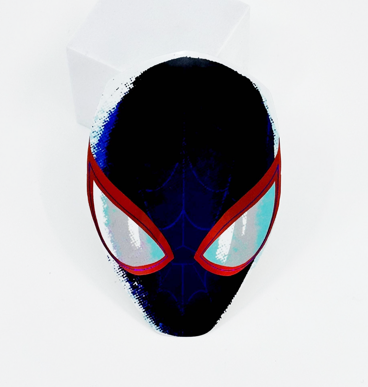 A Spider-Man themed paper mask with a black base, red eye borders, and light blue eyes, displayed on a white block against a white background.