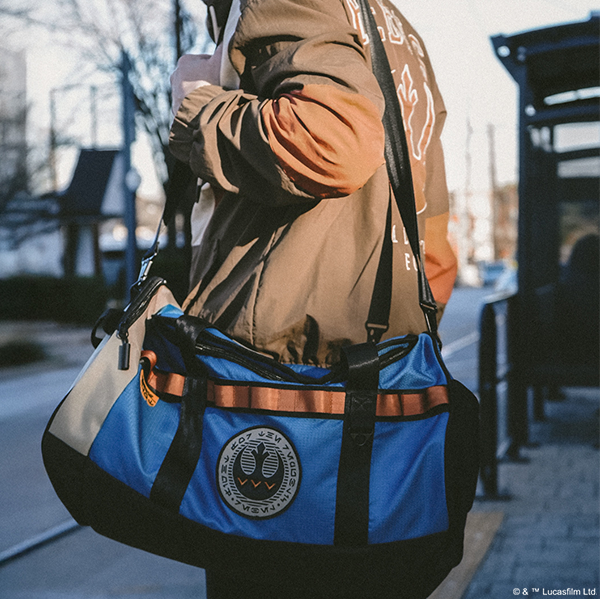 Person holding a blue and black bag with a logo, outdoors.